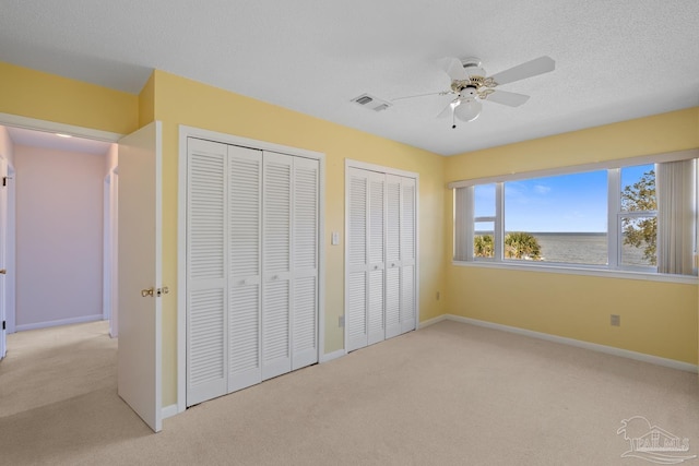 unfurnished bedroom with carpet, two closets, visible vents, and baseboards