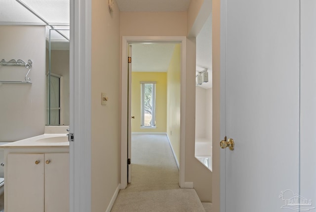 corridor featuring light colored carpet, a sink, and baseboards