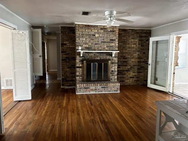 unfurnished living room with ceiling fan, crown molding, brick wall, a brick fireplace, and dark wood-type flooring