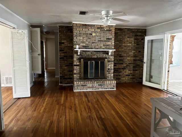 unfurnished living room featuring dark wood-style flooring, a brick fireplace, visible vents, and crown molding