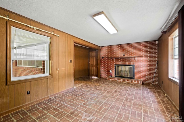 unfurnished living room featuring brick wall, a textured ceiling, a fireplace, and wood walls