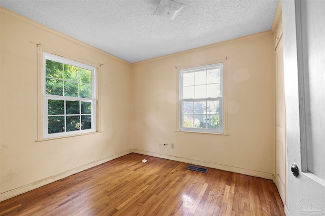 empty room with a healthy amount of sunlight, crown molding, wood-type flooring, and a textured ceiling