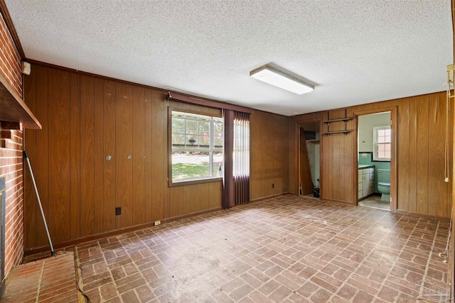 spare room with a brick fireplace, a textured ceiling, and wood walls