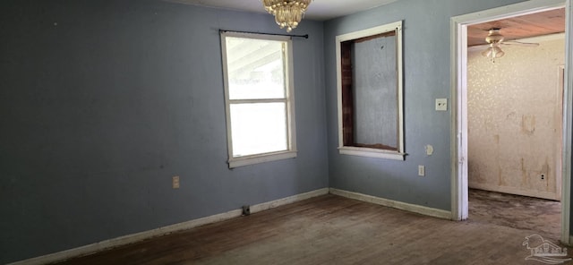 empty room with ceiling fan with notable chandelier, baseboards, and wood finished floors