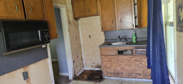 kitchen with brown cabinetry, baseboards, black microwave, and a sink