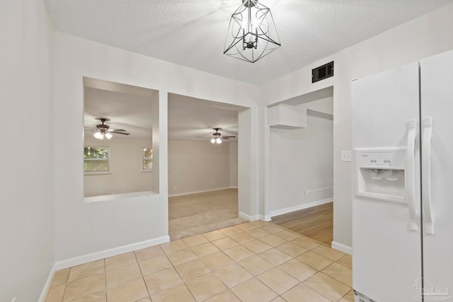 unfurnished dining area with ceiling fan with notable chandelier, light tile patterned floors, and a textured ceiling