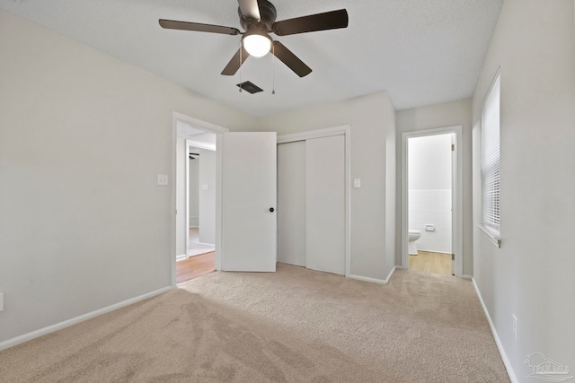 unfurnished bedroom with light carpet, a closet, ensuite bathroom, and ceiling fan