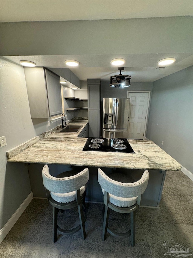 kitchen with stainless steel fridge, a breakfast bar, a peninsula, black electric cooktop, and gray cabinets