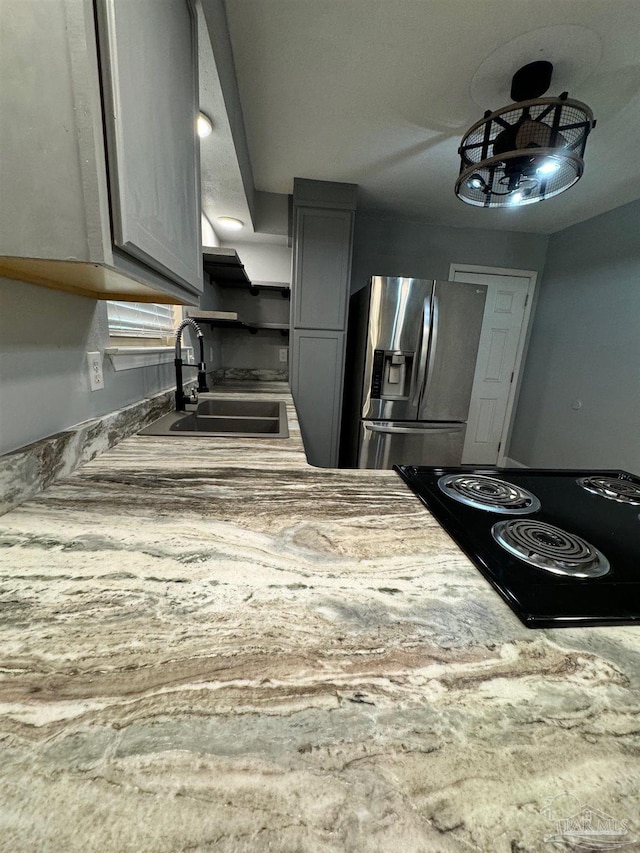 kitchen with gray cabinets, light countertops, black cooktop, a sink, and stainless steel fridge