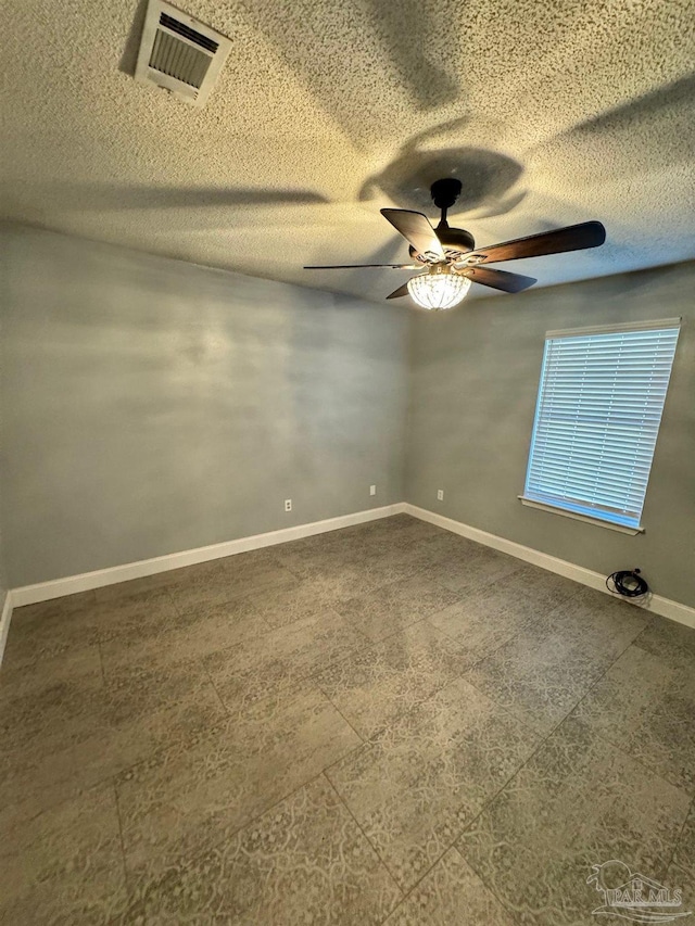 empty room with a textured ceiling, ceiling fan, visible vents, and baseboards