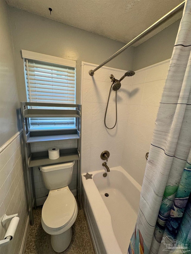 bathroom with tile walls, toilet, shower / bath combo with shower curtain, wainscoting, and a textured ceiling