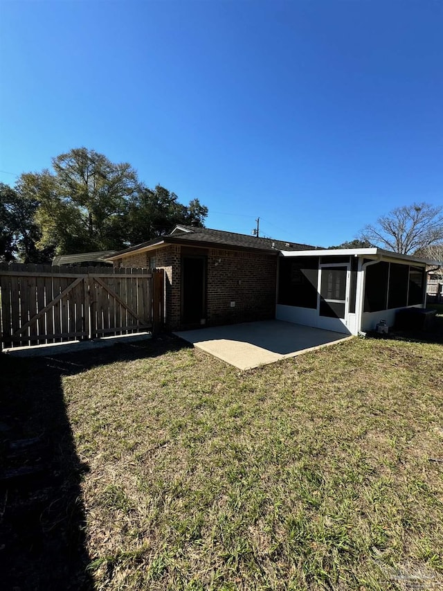 back of house featuring a patio area, a lawn, fence, and a sunroom