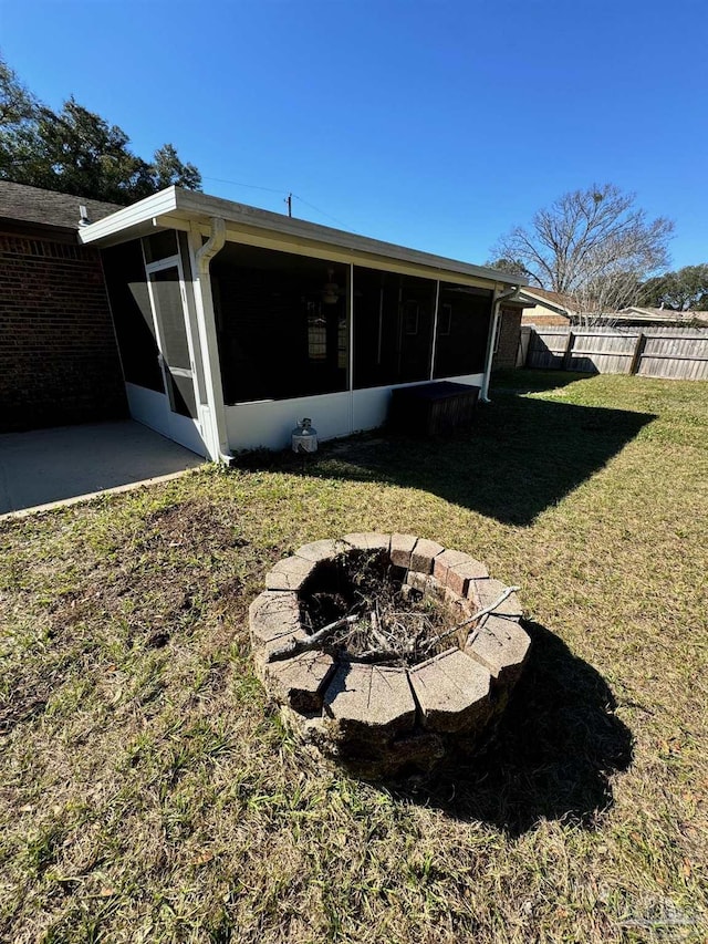 rear view of house featuring a sunroom, fence, a fire pit, and a lawn