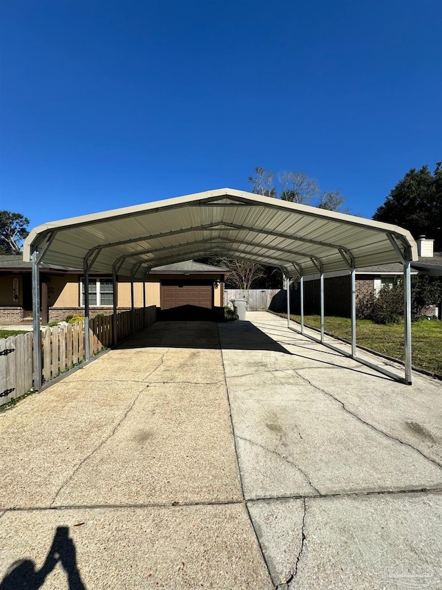 view of parking / parking lot featuring a carport, concrete driveway, and fence