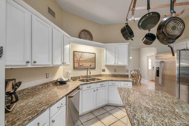 kitchen with light tile patterned floors, white cabinets, light stone counters, appliances with stainless steel finishes, and sink