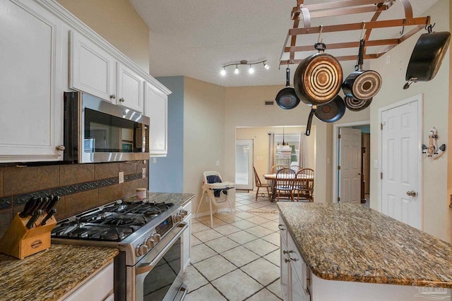 kitchen with light tile patterned flooring, white cabinetry, backsplash, a kitchen island, and appliances with stainless steel finishes