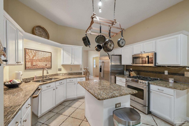 kitchen with appliances with stainless steel finishes, sink, stone countertops, a kitchen island, and white cabinets