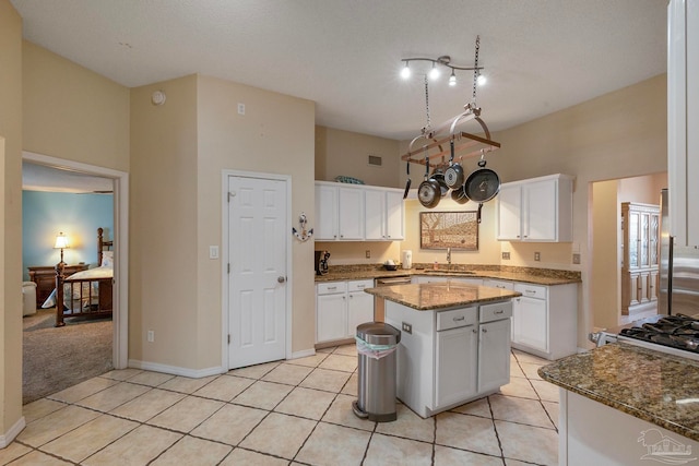 kitchen with stone counters, sink, a kitchen island, light tile patterned flooring, and white cabinetry