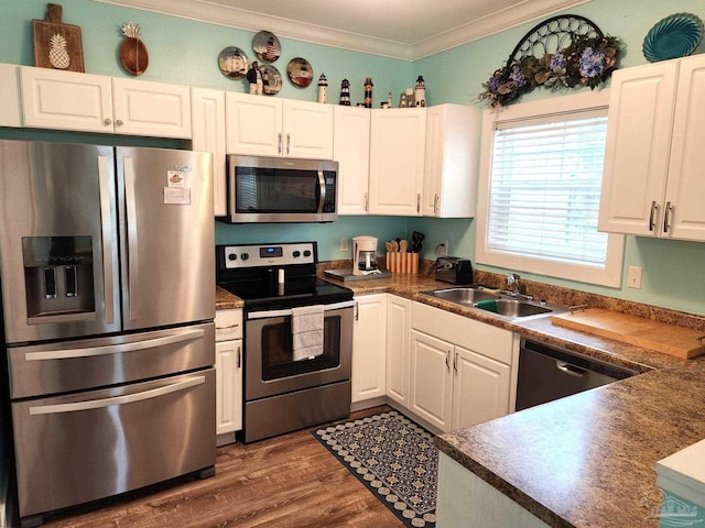 kitchen featuring dark wood-type flooring, a sink, white cabinets, ornamental molding, and appliances with stainless steel finishes