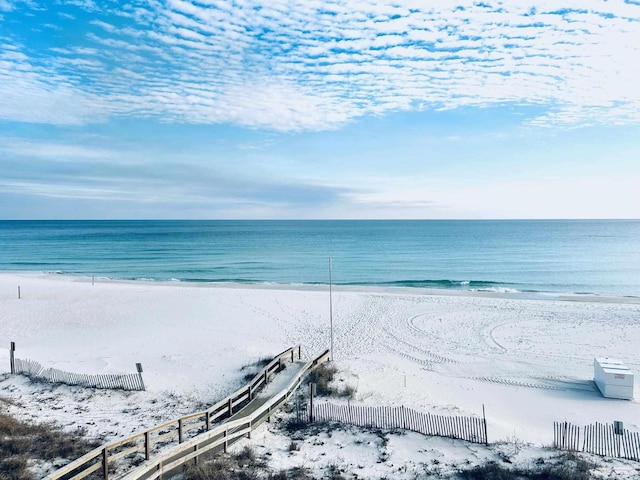 water view featuring fence and a beach view