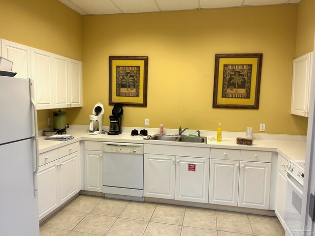 kitchen with a paneled ceiling, light tile patterned flooring, a sink, white cabinets, and white appliances