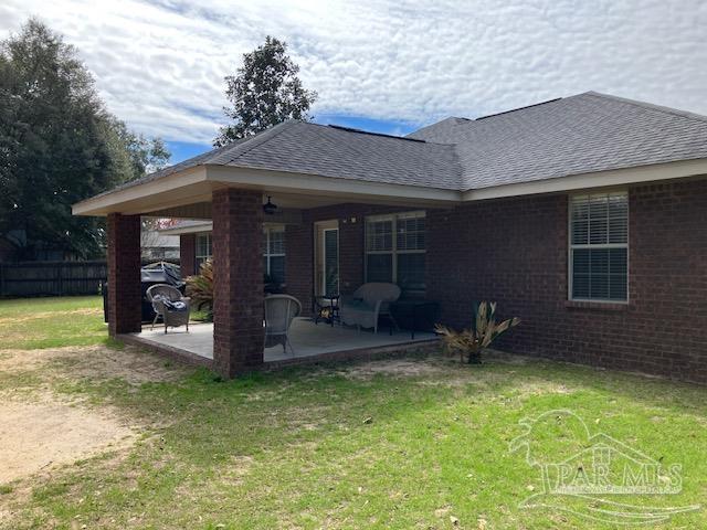 back of house with brick siding, a lawn, fence, and roof with shingles