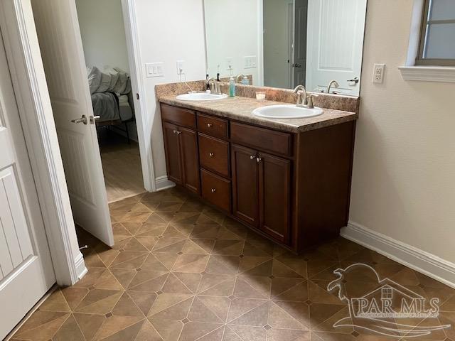 ensuite bathroom with double vanity, tile patterned flooring, a sink, and baseboards