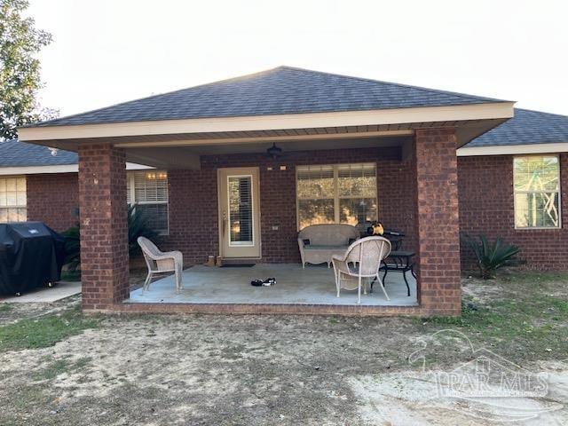 rear view of house with brick siding, a patio, and roof with shingles