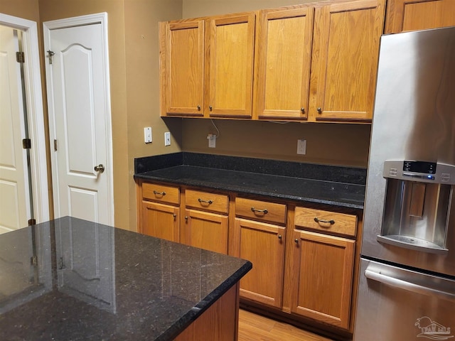 kitchen featuring dark stone countertops, light hardwood / wood-style flooring, and stainless steel refrigerator with ice dispenser