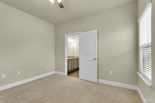 unfurnished bedroom with multiple windows, ensuite bathroom, carpet floors, and ceiling fan