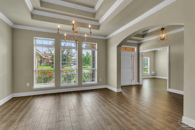 unfurnished room with arched walkways, a tray ceiling, wood finished floors, and crown molding