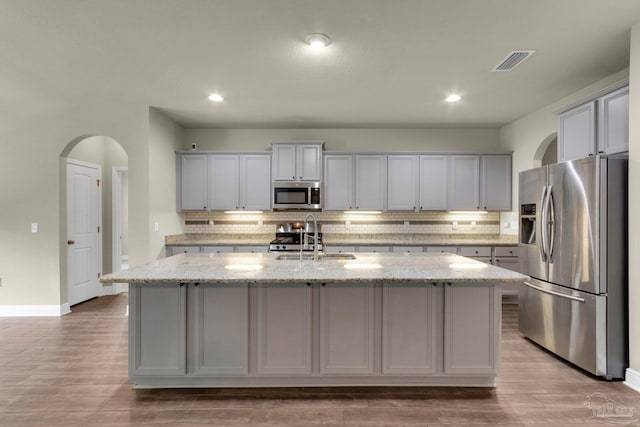 kitchen featuring appliances with stainless steel finishes, light stone counters, hardwood / wood-style flooring, and backsplash