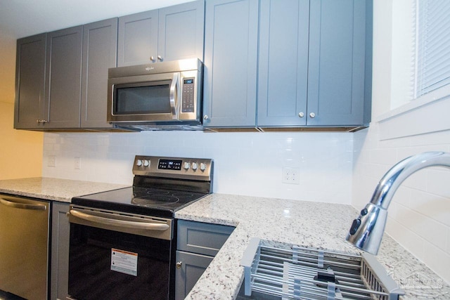 kitchen with appliances with stainless steel finishes, light stone counters, and decorative backsplash