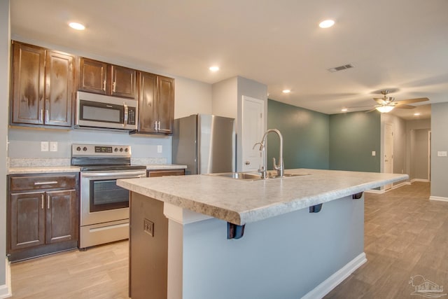 kitchen with ceiling fan, a kitchen bar, a kitchen island with sink, and appliances with stainless steel finishes