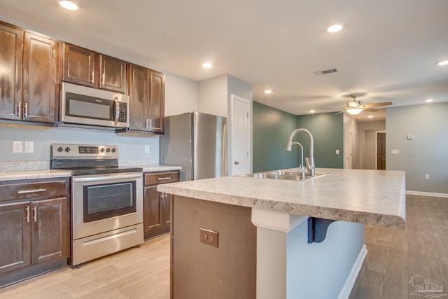 kitchen with a center island with sink, ceiling fan, light wood-type flooring, appliances with stainless steel finishes, and a breakfast bar area