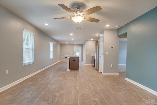 kitchen with sink, ceiling fan, light wood-type flooring, an island with sink, and stainless steel refrigerator