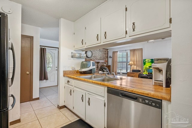 kitchen featuring stainless steel dishwasher, a sink, light tile patterned floors, white cabinetry, and freestanding refrigerator