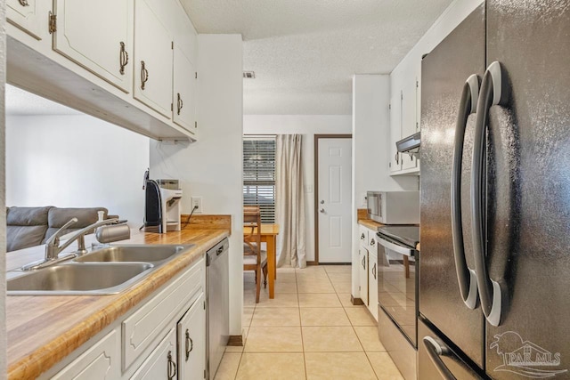 kitchen with stainless steel appliances, a sink, white cabinetry, and light tile patterned flooring
