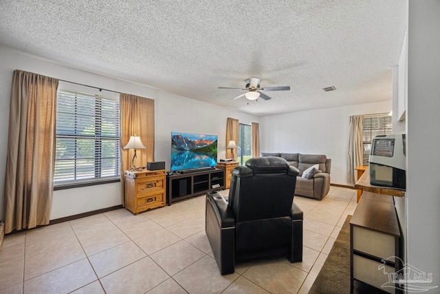 living area featuring a textured ceiling, light tile patterned flooring, ceiling fan, baseboards, and visible vents
