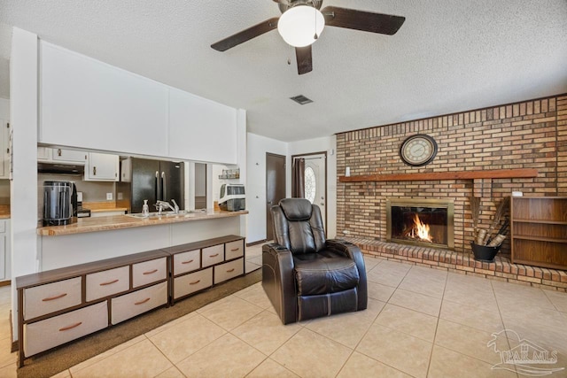 living room featuring a ceiling fan, a textured ceiling, light tile patterned floors, a fireplace, and visible vents