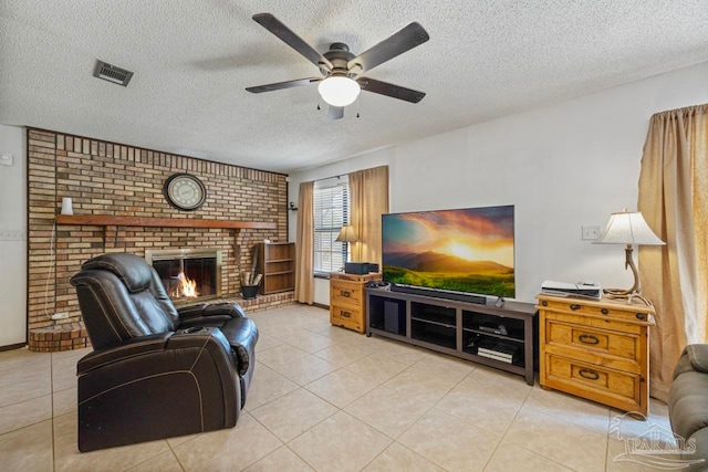 living room with a textured ceiling, light tile patterned flooring, visible vents, a ceiling fan, and a brick fireplace