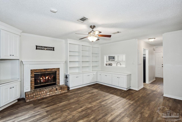 unfurnished living room with a fireplace, crown molding, dark hardwood / wood-style floors, ceiling fan, and a textured ceiling