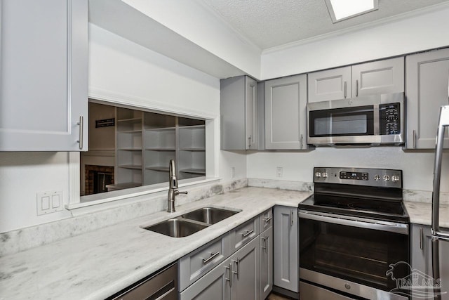 kitchen with a textured ceiling, appliances with stainless steel finishes, sink, gray cabinets, and ornamental molding