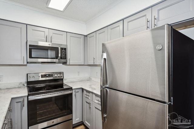 kitchen with ornamental molding, a textured ceiling, stainless steel appliances, and gray cabinetry