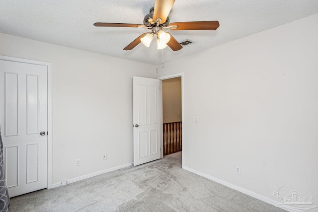 empty room with ceiling fan, light carpet, and a textured ceiling