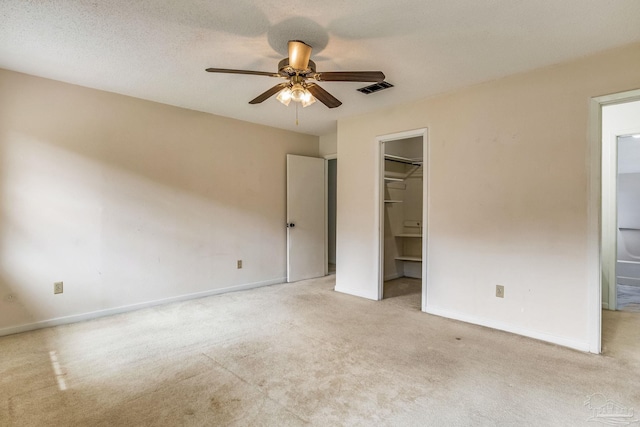 unfurnished bedroom with ceiling fan, a walk in closet, light carpet, a closet, and ensuite bath