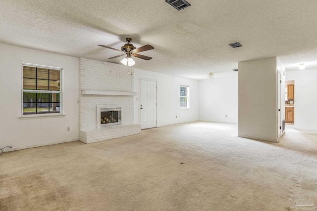 unfurnished living room with a fireplace, a textured ceiling, light carpet, ceiling fan, and brick wall