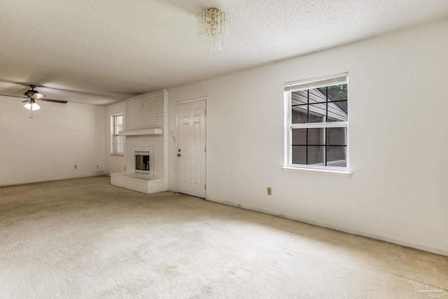 unfurnished living room featuring ceiling fan, brick wall, light colored carpet, a fireplace, and a textured ceiling