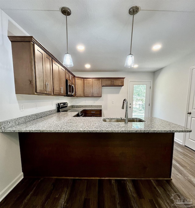 kitchen with light stone countertops, dark wood finished floors, a peninsula, a sink, and appliances with stainless steel finishes