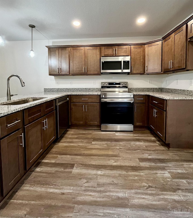 kitchen with a sink, hanging light fixtures, wood finished floors, and stainless steel appliances